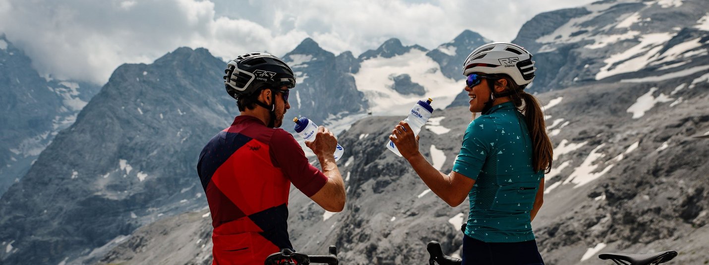 Two cyclists drinking water with mountain scenery in the background