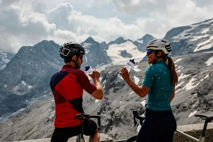Zwei Radfahrer trinken Wasser mit Bergpanorama im Hintergrund