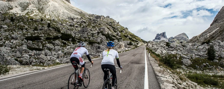 Warum Alta Badia auf jede Roadbike-Bucket-List gehört © Paola Finali Zwei Radfahrer fahren eine Bergstraße mit Felsen und wolkigem Himmel.