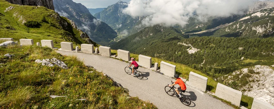 Due ciclisti su strada di montagna con vista sulle montagne e nuvole