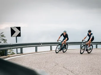 Sterzing © Jens Scheibe Two cyclists riding on a winding mountain road under cloudy sky