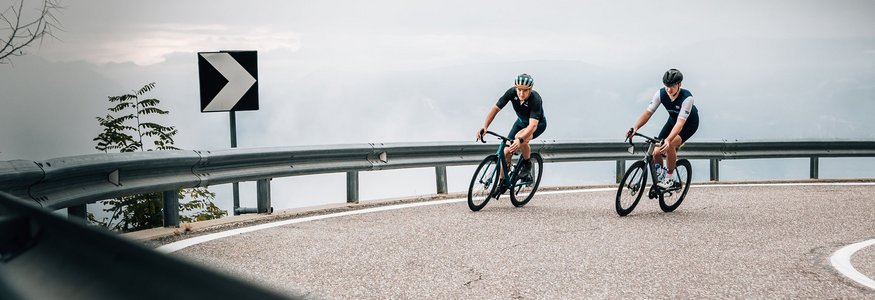 Zwei Radfahrer fahren auf einer kurvigen Bergstraße bei bewölktem Himmel