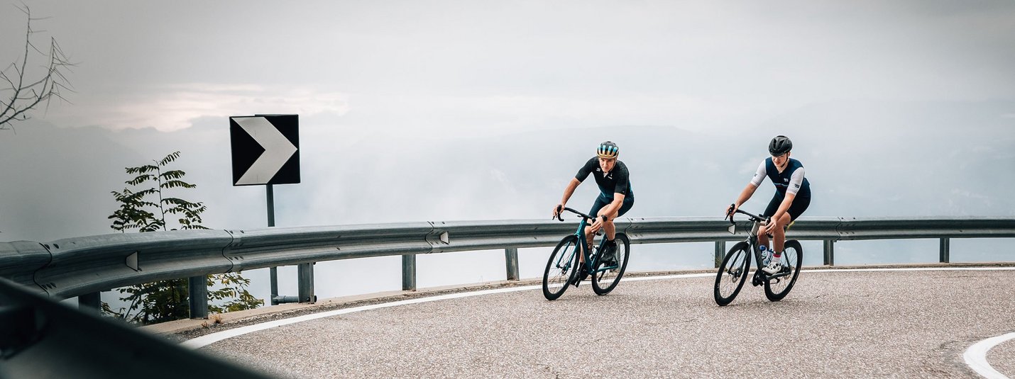 Twee fietsers op een kronkelende bergweg bij bewolkte lucht