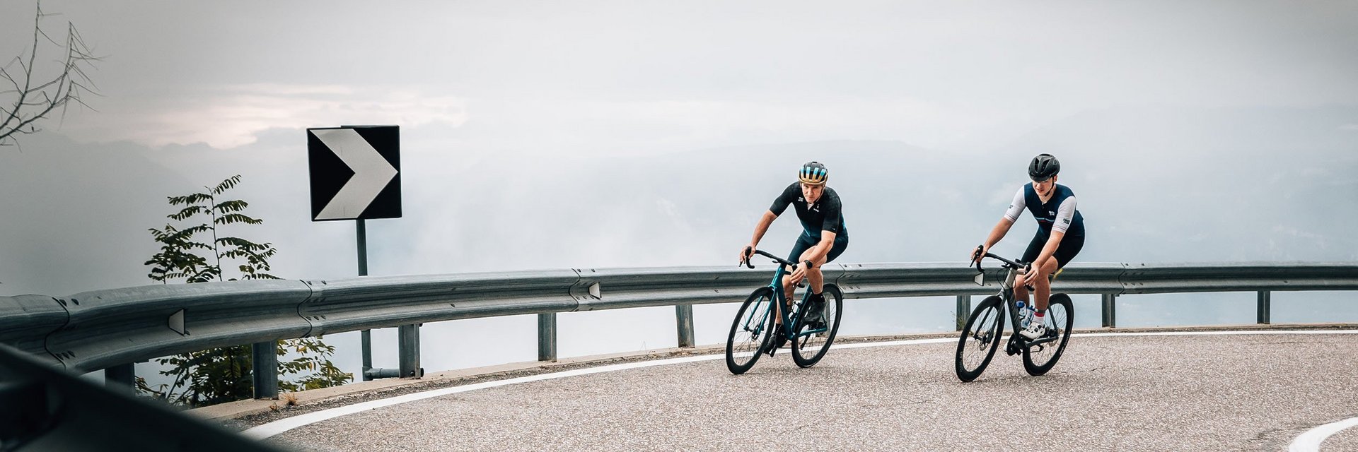 Twee fietsers op een kronkelende bergweg bij bewolkte lucht