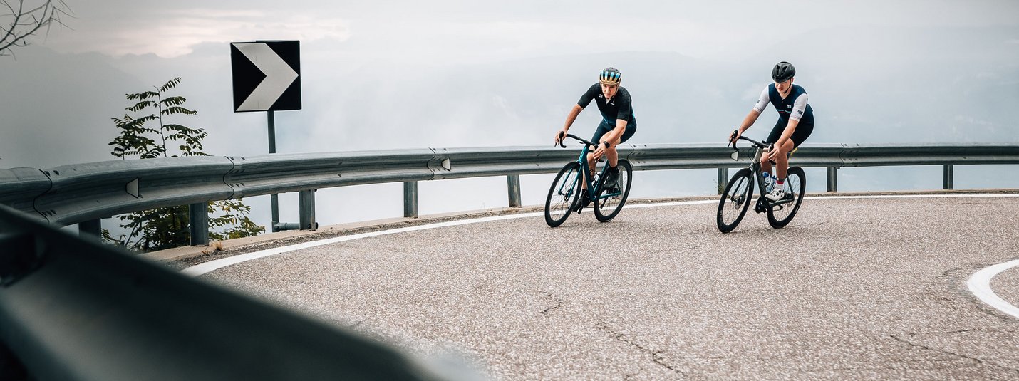 Tramin - Mendelpass © Jens Scheibe Zwei Radfahrer fahren auf einer kurvigen Bergstraße bei bewölktem Himmel
