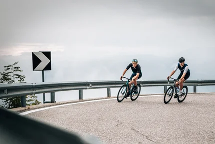 Twee fietsers op een kronkelende bergweg bij bewolkte lucht