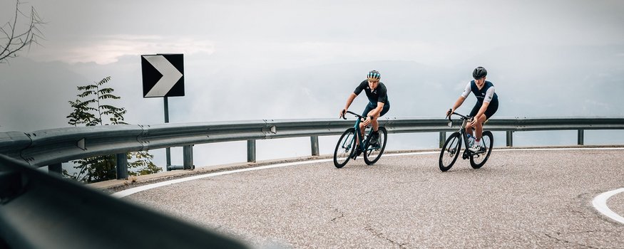 Rennrad Urlaub in Südtirol © Jens Scheibe Zwei Radfahrer fahren auf einer kurvigen Bergstraße bei bewölktem Himmel