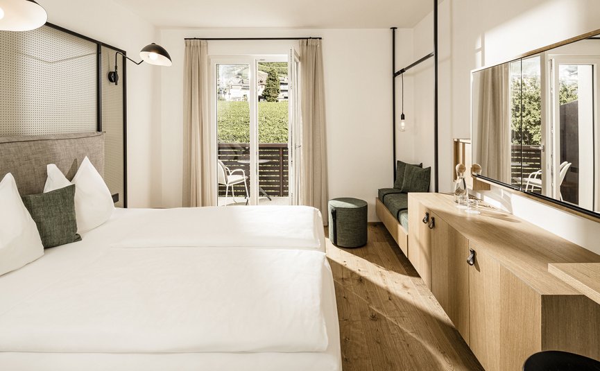 Camera d'hotel luminosa con letto matrimoniale, balcone e arredamento in legno moderno