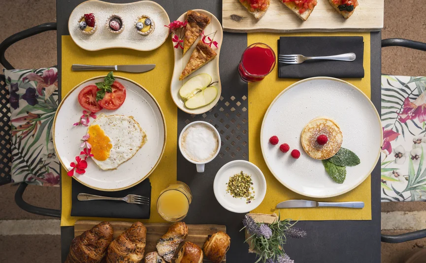 Frühstück mit Spiegelei, Pfannkuchen, Croissants, Obst und Getränken auf Tisch