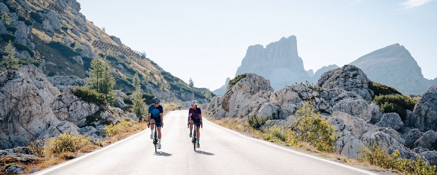 Italiens Pässeparadies © Josef Plaickner Zwei Radfahrer fahren auf Bergstraße mit Felsen und Gipfeln im Hintergrund