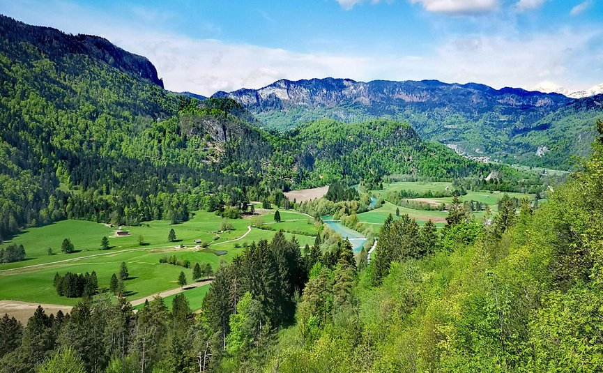 Valle verde con fiume e montagne boschive sotto cielo azzurro