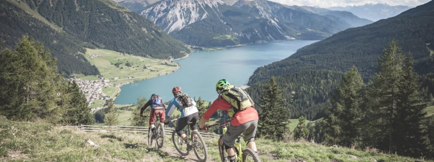 Tre mountain biker su un sentiero con vista sul lago e sulle montagne