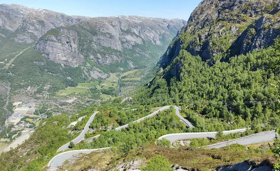 Serpentinenstraße im bergigen, grünen Tal bei klarem Himmel