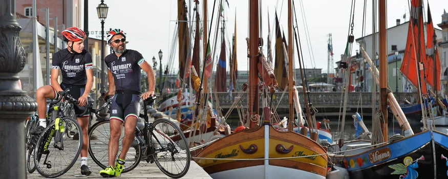 Twee wielrenners in sportkleding staan met fietsen bij haven met kleurrijke boten
