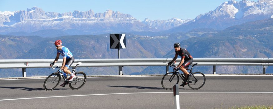 Hotel Teutschhaus ***S © Hotel Teutschhaus Kurtinig Two cyclists on a winding mountain road with snowy peaks in the background
