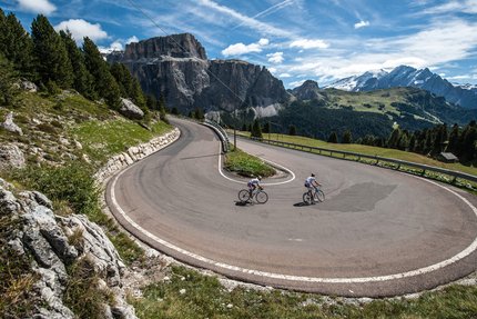 Cyclists riding sharp hairpin bend on mountain road with scenic views