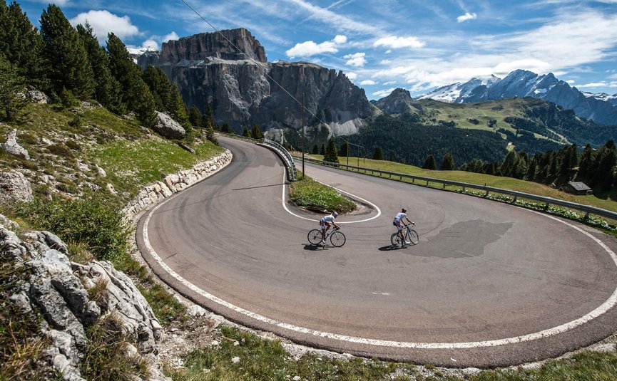 Cyclists riding sharp hairpin bend on mountain road with scenic views