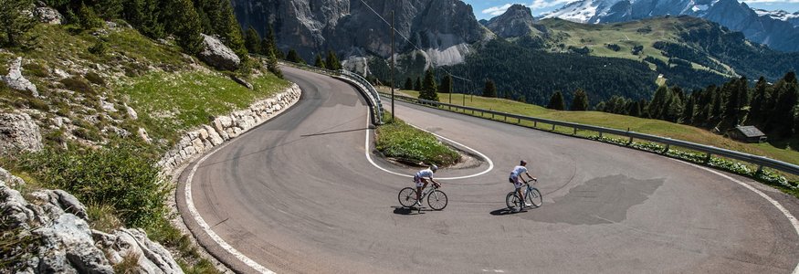 Cyclists riding sharp hairpin bend on mountain road with scenic views