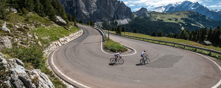 Alta Badia © Paola Finali Radfahrer fahren enge Haarnadelkurve in bergiger Landschaft bei klarem Himmel