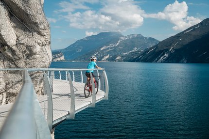 Fietser op wandelpad met uitzicht op meer en bergen bij zonnig weer