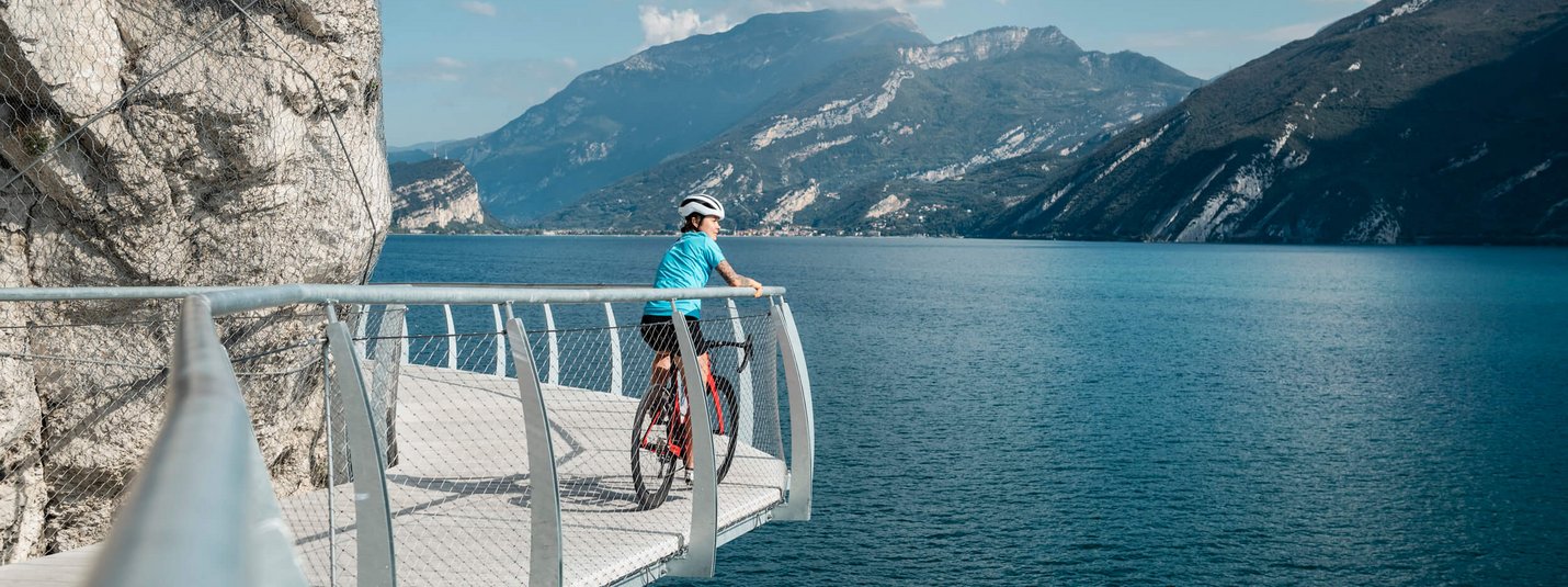 Cyclist on a walkway overlooking lake and mountains on a sunny day