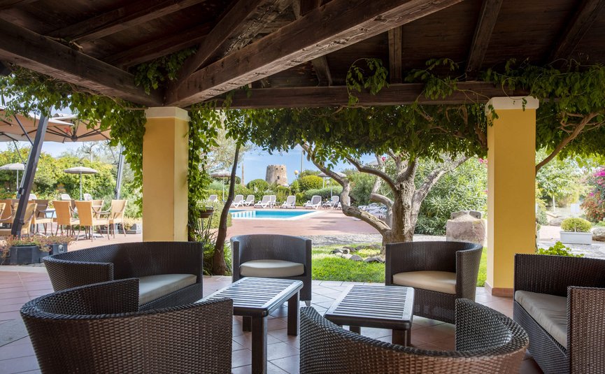 Covered seating area with lounge furniture overlooking pool and garden