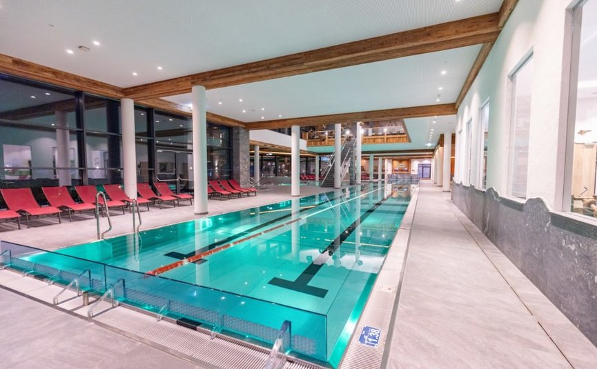 Piscina interna moderna con sedie rosse e travi in legno