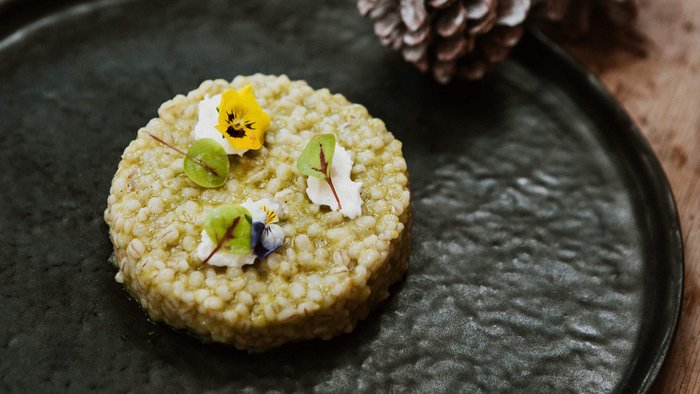 Runder Gerichte mit essbaren Blumen und grünen Blättern auf schwarzem Teller