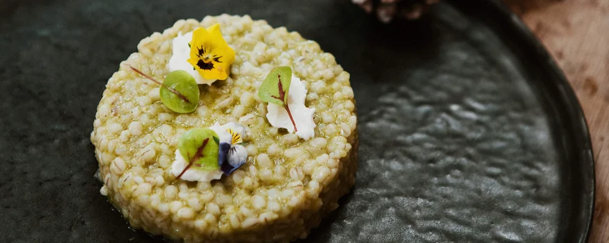 Runder Gerichte mit essbaren Blumen und grünen Blättern auf schwarzem Teller
