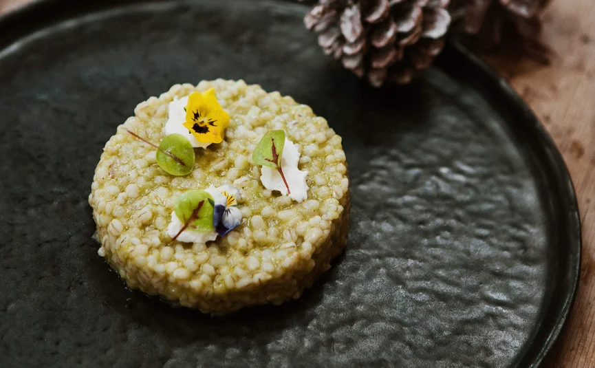 Runder Gerichte mit essbaren Blumen und grünen Blättern auf schwarzem Teller
