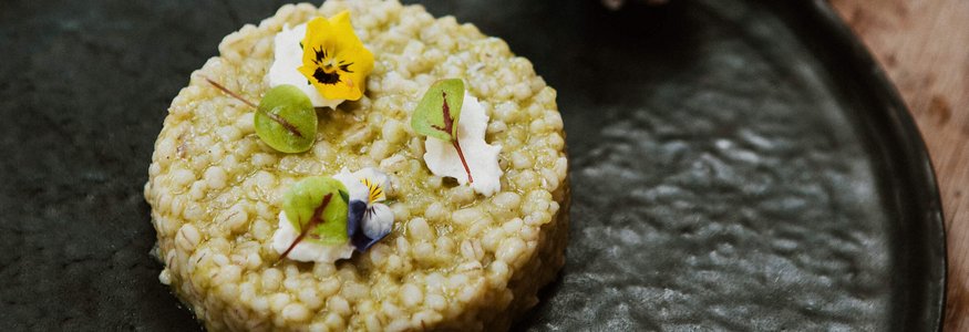 Runder Gerichte mit essbaren Blumen und grünen Blättern auf schwarzem Teller