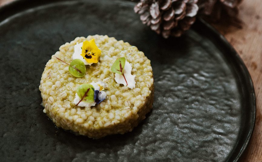 Runder Gerichte mit essbaren Blumen und grünen Blättern auf schwarzem Teller