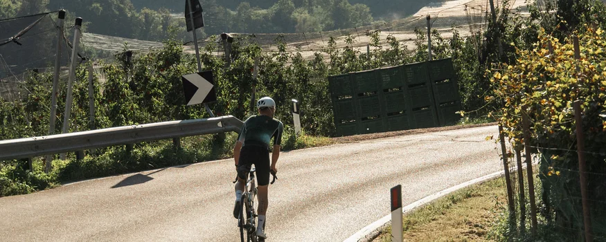 Ein Rennrad-Wochenende in Südtirols Süden © marc.moves x velysiped Radfahrer auf einer kurvigen Landstraße mit Bergen im Hintergrund