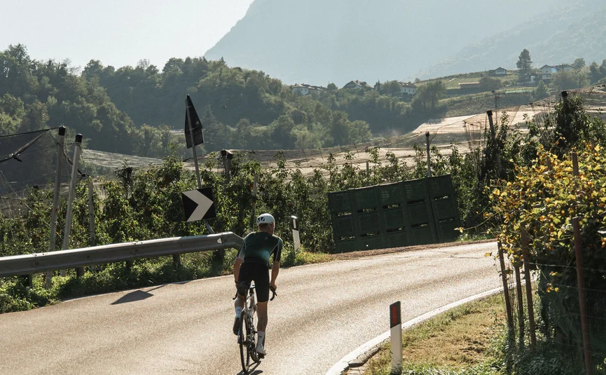 Ciclista su una strada di campagna tortuosa con montagne sullo sfondo