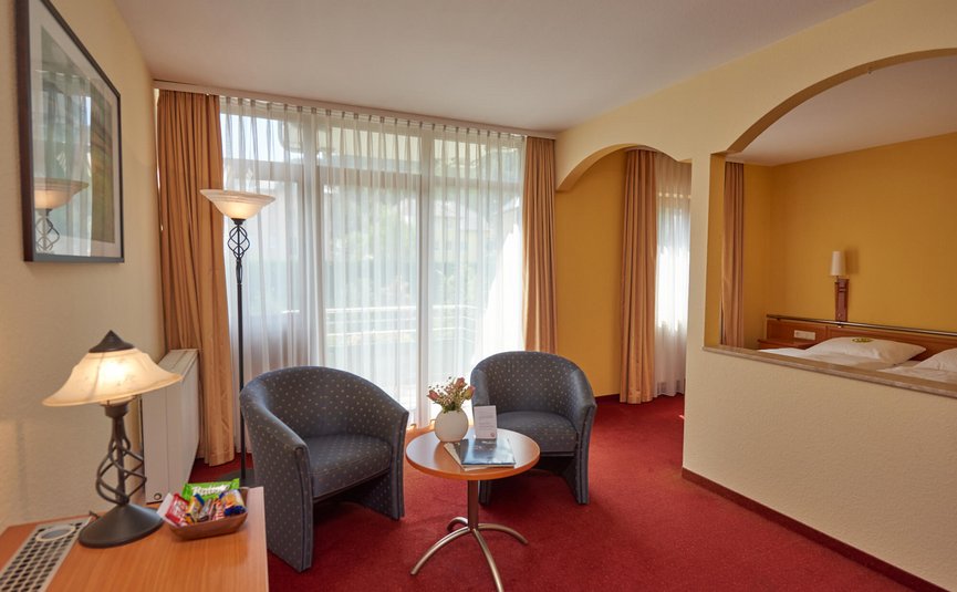 Camera d'albergo luminosa con zona salotto, due poltrone e accesso al balcone