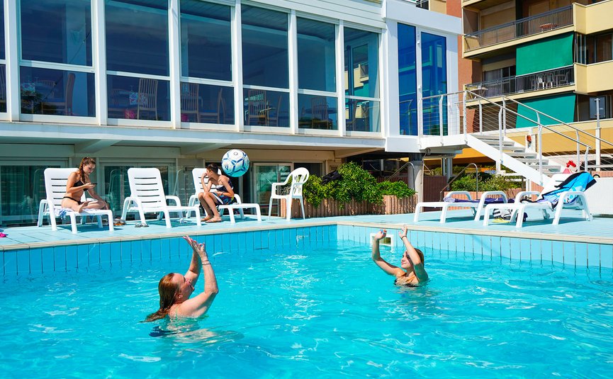 Persone che giocano con pallone in piscina all'aperto vicino a terrazza