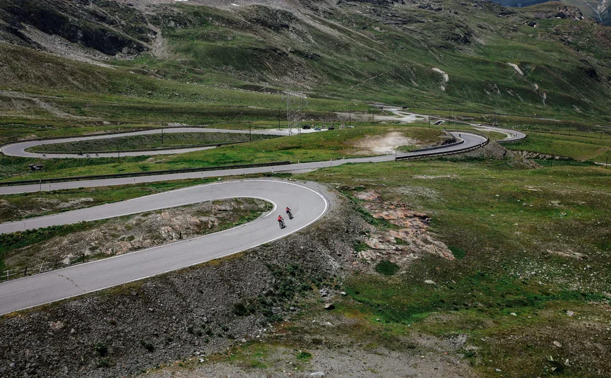 Two cyclists on winding mountain road in green landscape