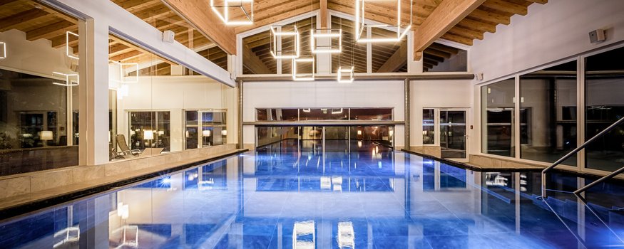 Binnenzwembad met houten plafond en geometrische lampen in lichte omgeving