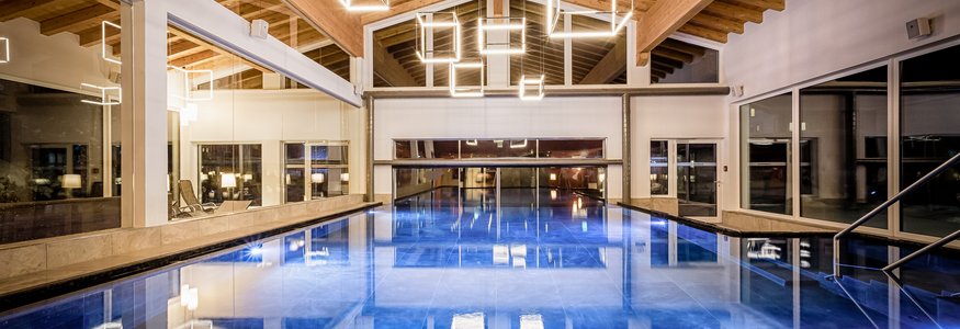 Interior view of a lit indoor swimming pool with wooden ceiling and geometric lights