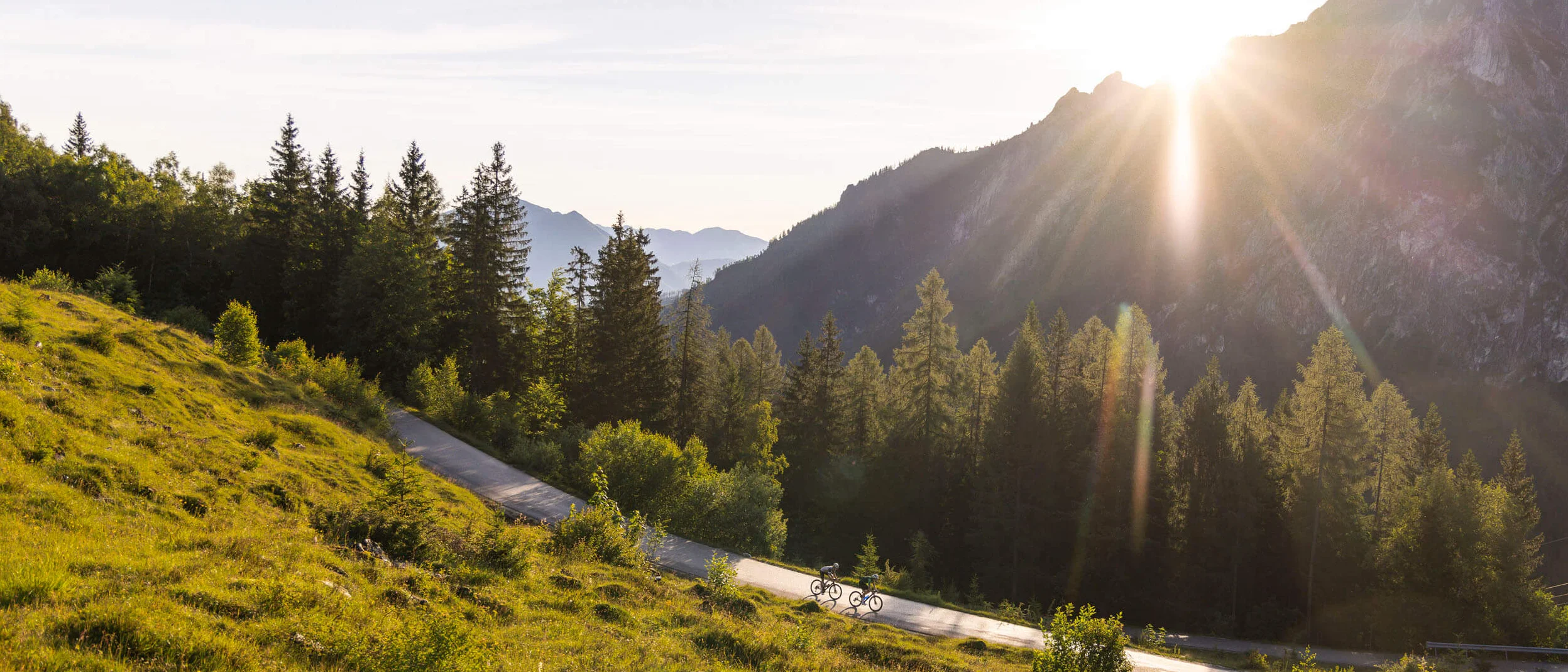 Ein Rennrad-Wochenende im SalzburgerLand – Salzkammergut © Heiko Mandl Radfahrer fahren bei Sonnenuntergang auf einer Bergstraße durch grüne Landschaft