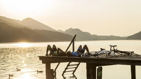 Ein Rennrad-Wochenende im SalzburgerLand – Salzkammergut © SalzburgerLand Fuschlsee - Markus Greber Zwei Radfahrer liegen auf Steg am See im Sonnenuntergang mit Fahrrädern