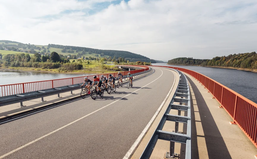 Gruppe von Radfahrern fährt über Brücke neben Fluss und grüner Landschaft