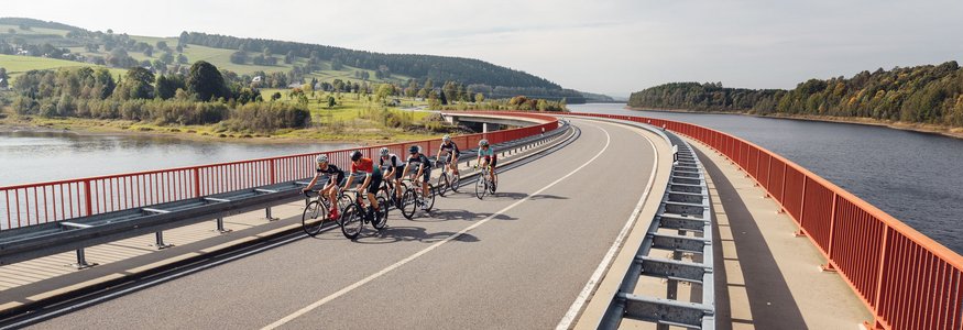 Gruppo di ciclisti su un ponte vicino a un fiume e paesaggio verde