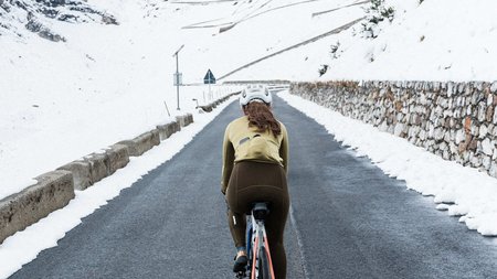 Radfahrerin auf bergiger Straße mit Schnee an den Seiten