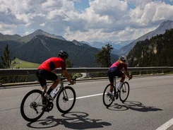 Two cyclists riding uphill on mountain road with cloudy sky
