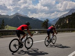 Due ciclisti in salita su strada di montagna con cielo nuvoloso
