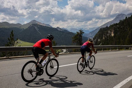 Due ciclisti in salita su strada di montagna con cielo nuvoloso
