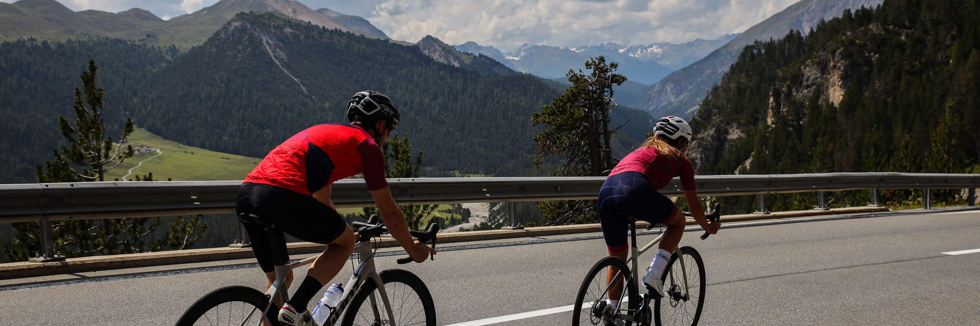 Twee wielrenners klimmen op bergweg met bergen en bewolkte lucht