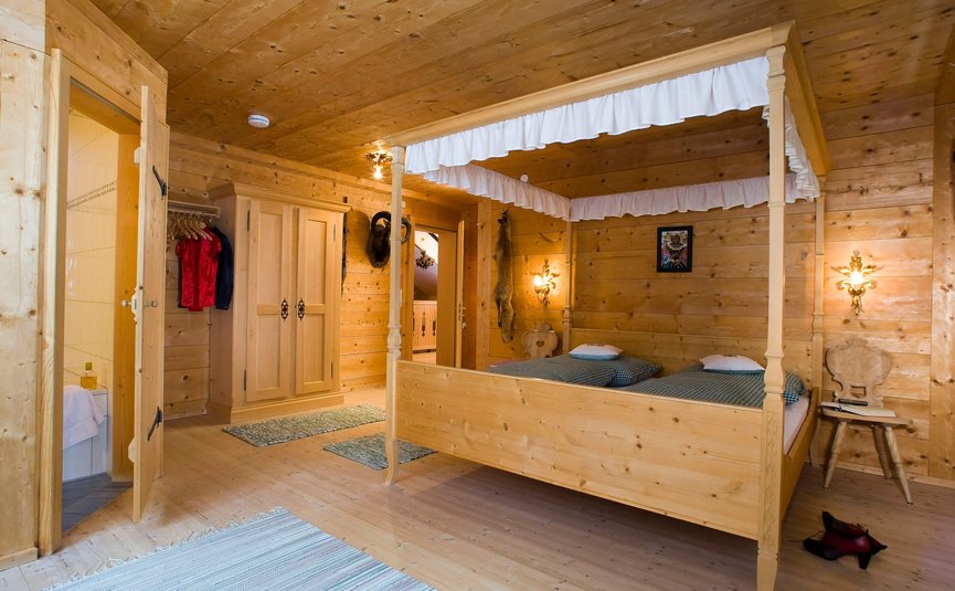 Zimmer mit Holzwänden, Himmelbett und offenem Eingang zum Badezimmer