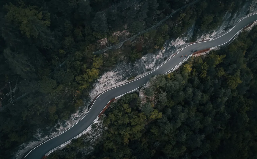 Mendelpass © Jens Scheibe Luftaufnahme einer kurvigen Bergstraße mit Radfahrern neben Wald